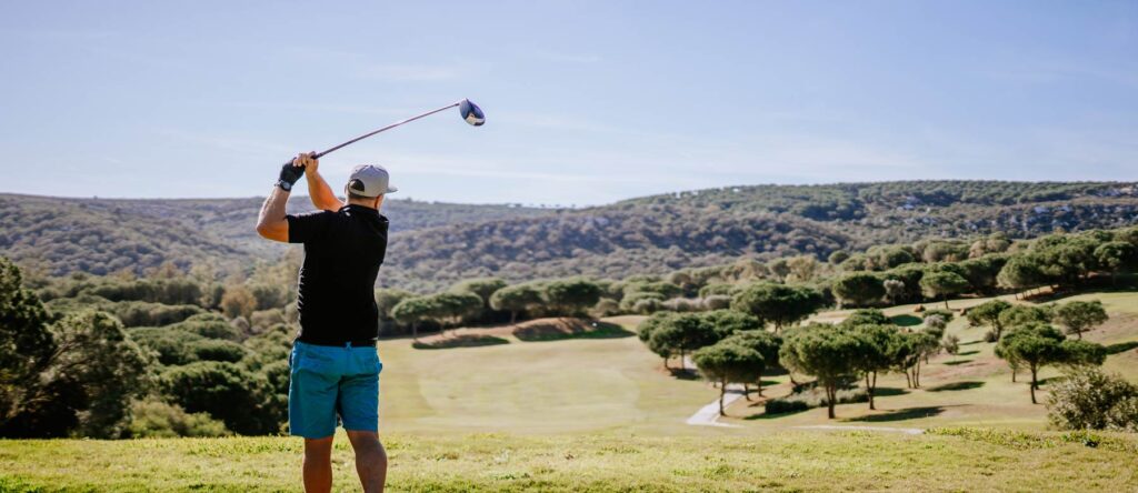 Golfer swinging a club on a scenic golf course.