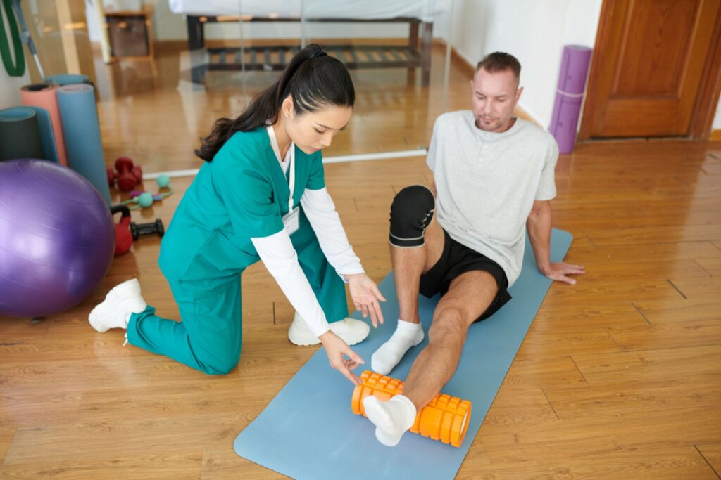 Physical therapist assisting a patient with ankle rehabilitation on a mat.