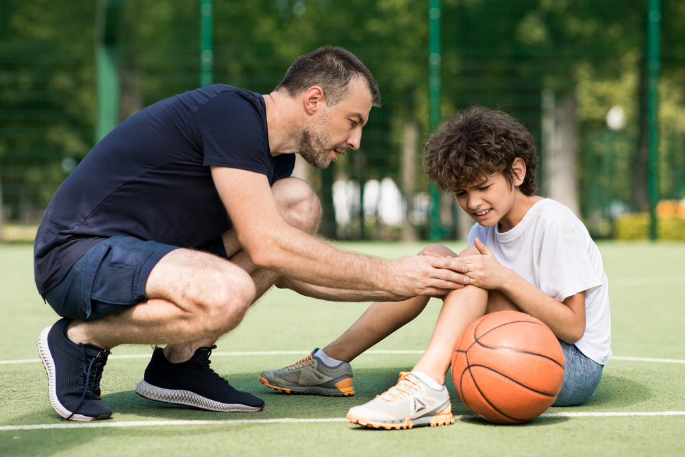 Adult tying a child’s shoelace on an outdoor court.