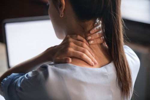 Person holding their neck, showing neck discomfort at a desk.